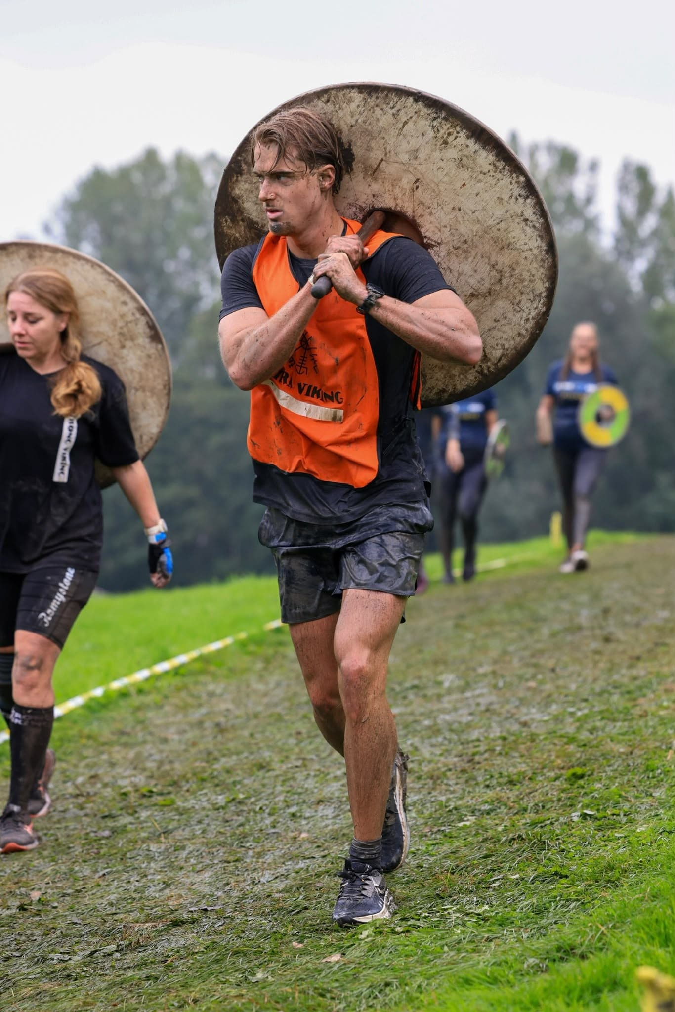 Teun draagt een grote ronde schijf op zijn schouder tijdens een wedstrijd buiten in het gras.